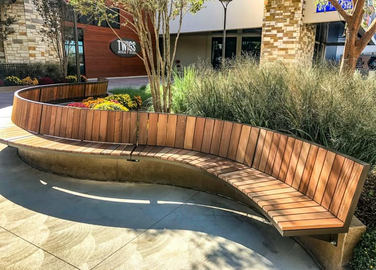 a wooden bench sitting on top of a sidewalk next to a planter filled with flowers