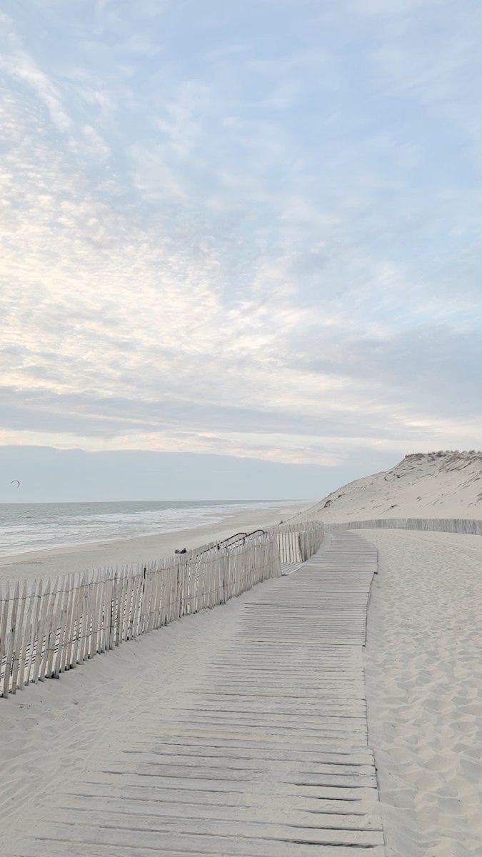 a wooden walkway leading to the beach with white sand and blue sky in the background