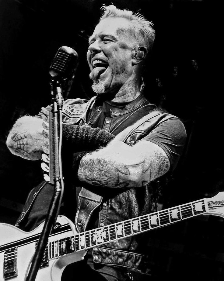 a black and white photo of a man singing into a microphone while playing an electric guitar