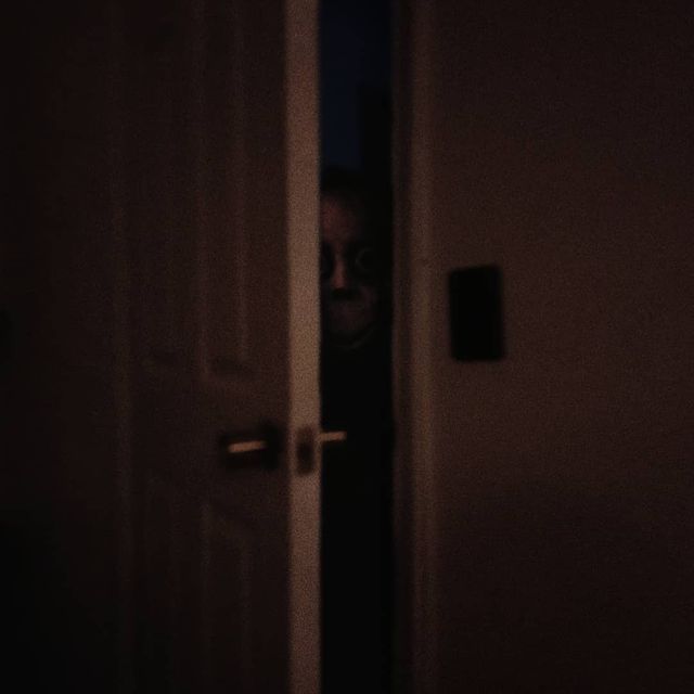 a person standing in front of a door with their face peeking through the doorway at night