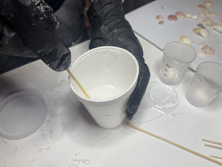 a person in black gloves is pouring something into a cup