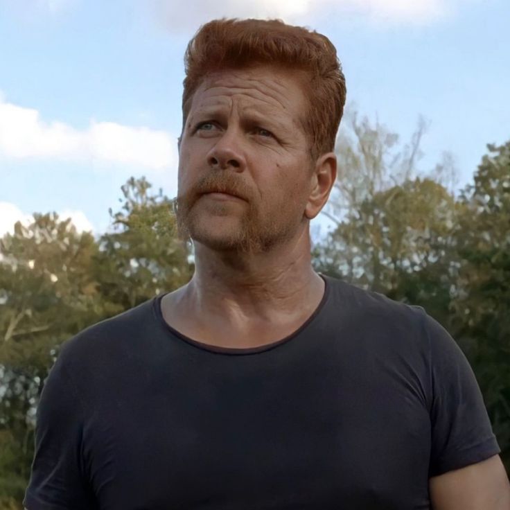 a close up of a person wearing a black t - shirt and trees in the background