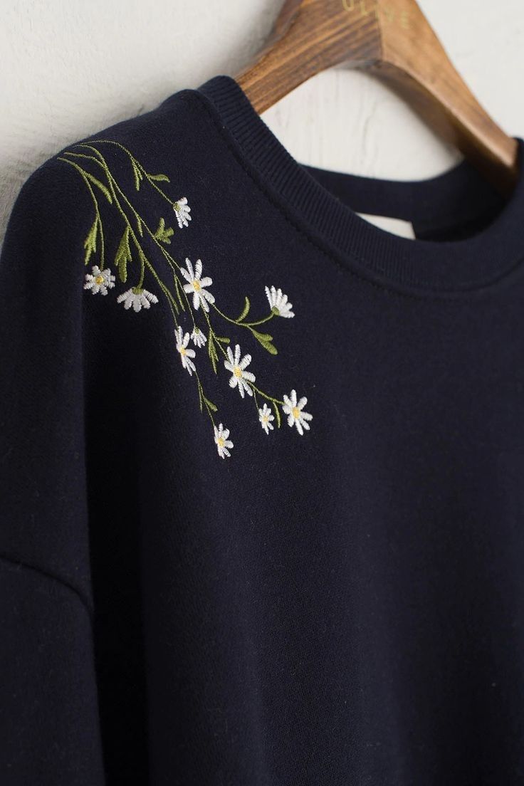 a black sweatshirt with daisies embroidered on the front and back, hanging from a wooden hanger