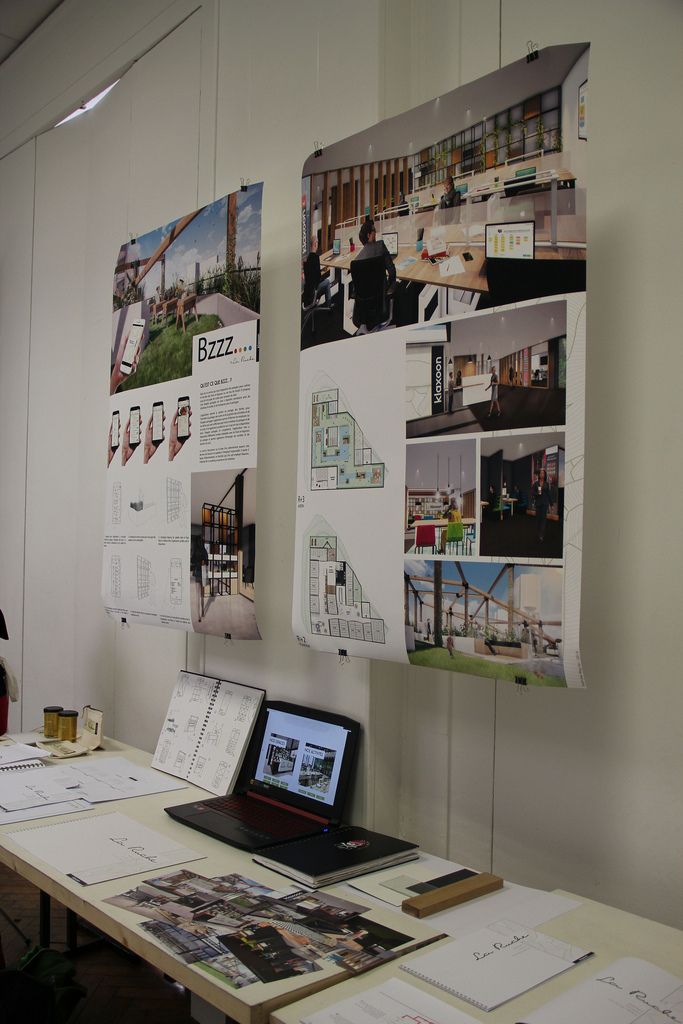 a laptop computer sitting on top of a wooden table next to papers and pictures hanging on the wall