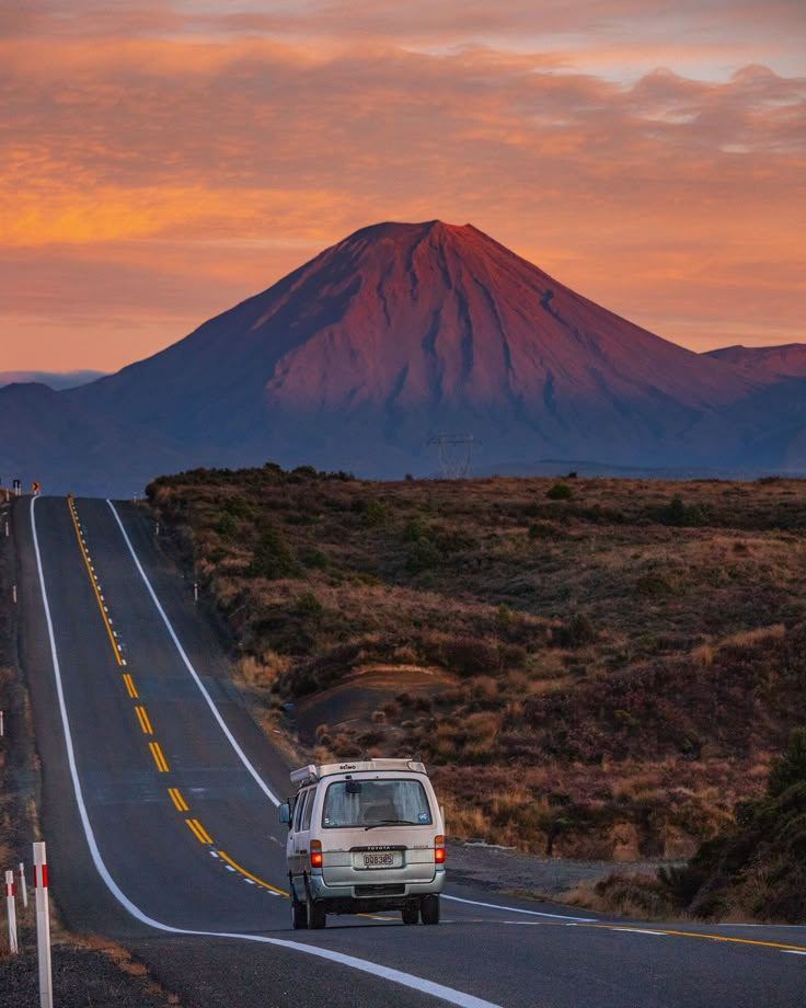 a van is driving down the road in front of a large mountain at sunset or sunrise