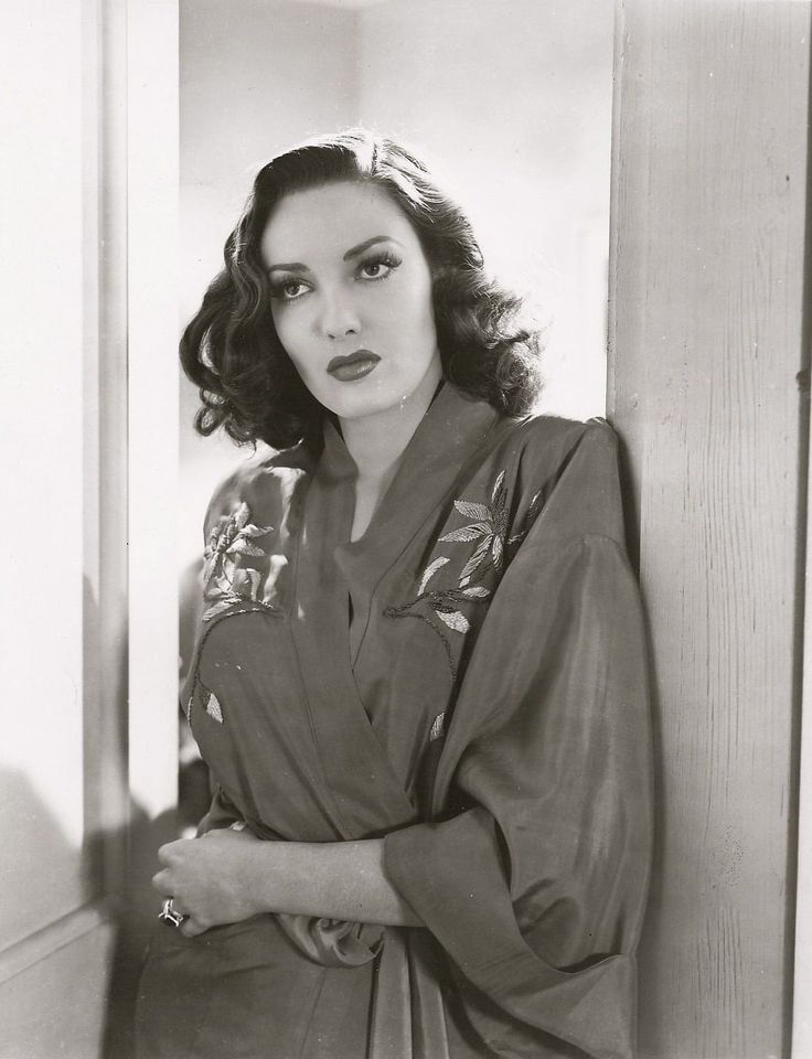 black and white photograph of a woman leaning against a wall with her hands on her hips