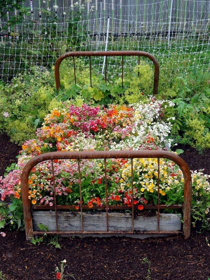 an old rusty bed frame with flowers growing in it and a wire fence behind it