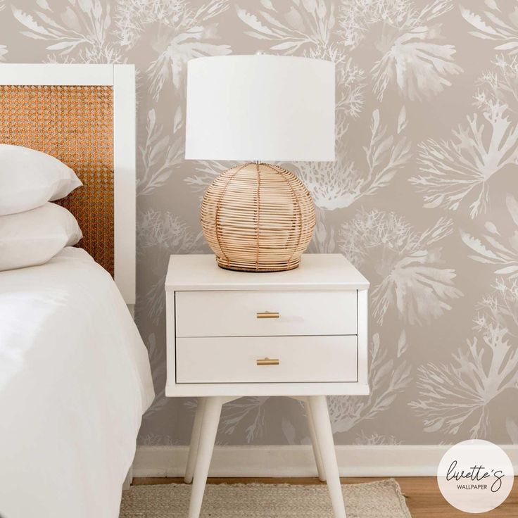 a nightstand with a lamp on it next to a bed and wallpapered walls