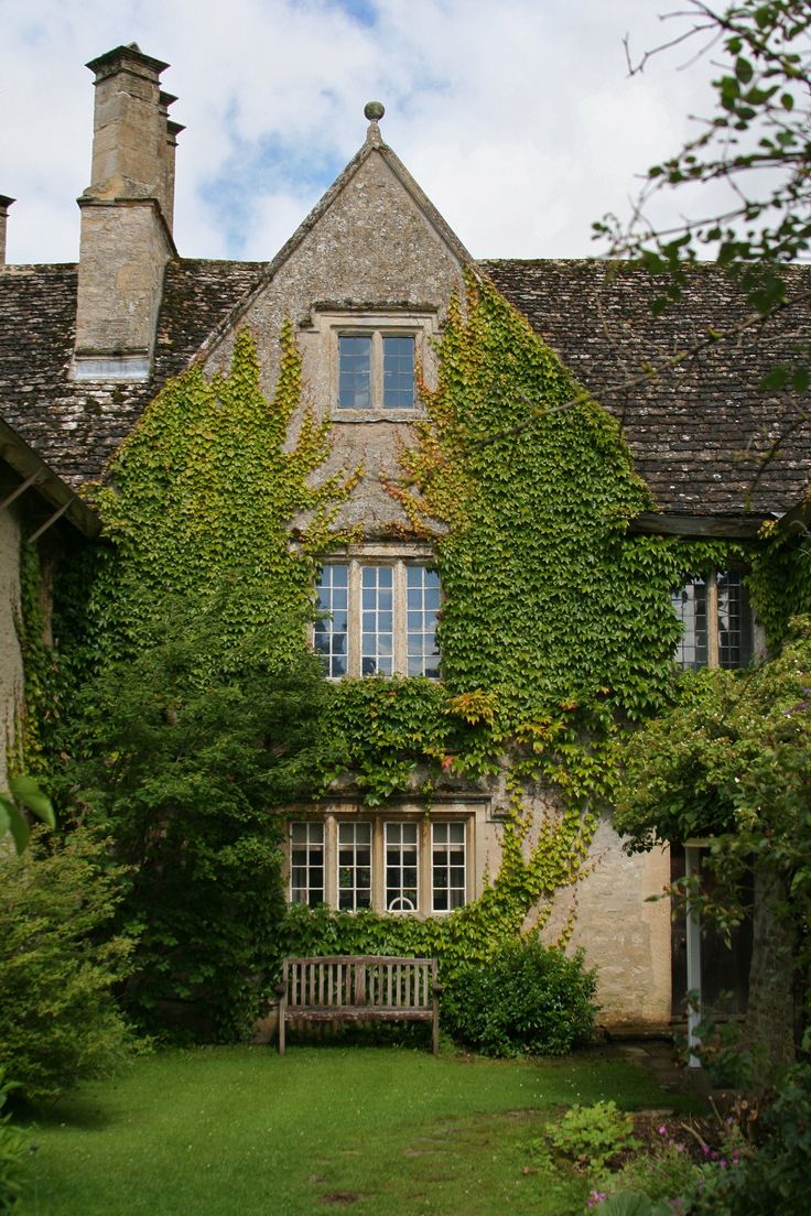 an old house covered in ivy with a bench next to the front door and windows