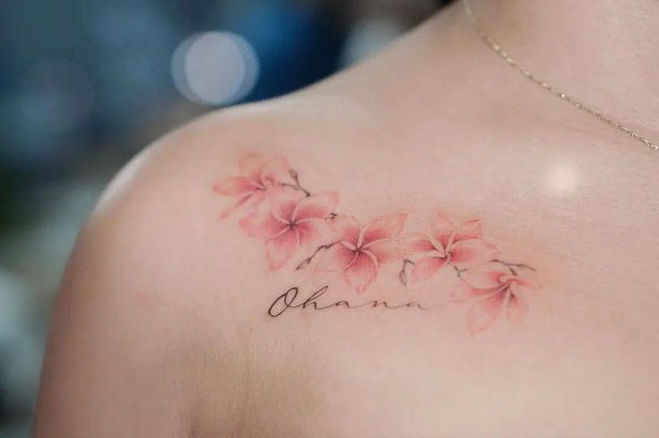 a woman's chest with pink flowers and the word ohana tattooed on it