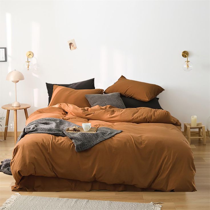 a bed with brown sheets and pillows in a white room next to a wooden floor