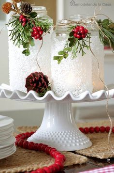 two mason jars with pine cones and berries on them are sitting on a cake plate