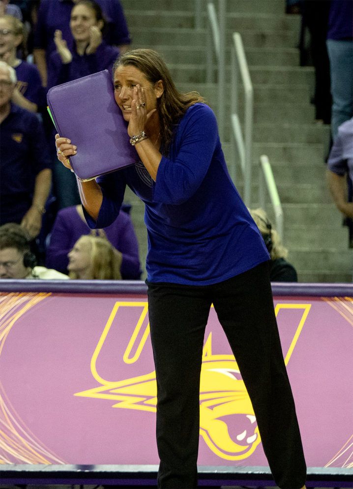 a woman holding a laptop in her right hand while standing on a court with other people watching