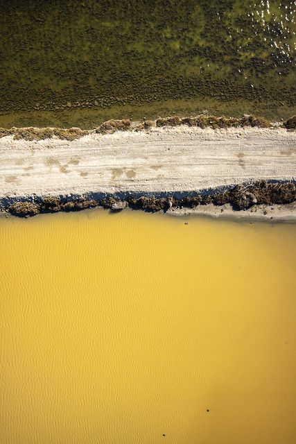 an aerial view of the beach and water from above, with yellow sand in the foreground