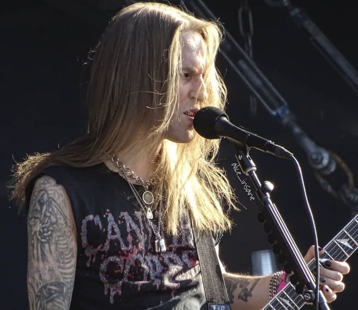 a man with long hair playing an electric guitar at a music festival in front of a microphone