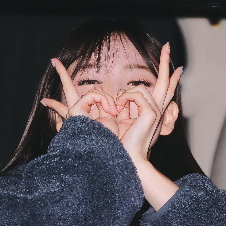 a woman covering her face with both hands and making the shape of a hand sign