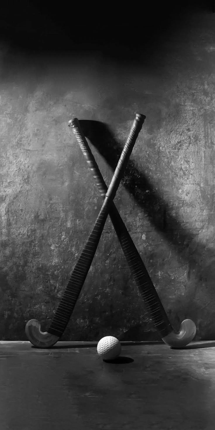 black and white photograph of two baseball bats leaning against a wall with a ball on the floor