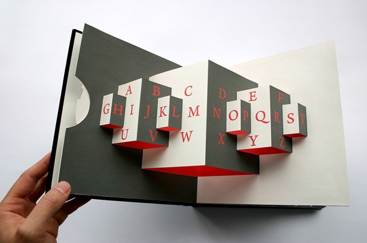 an open book with red and white letters on the front cover is being held up by a person's hand