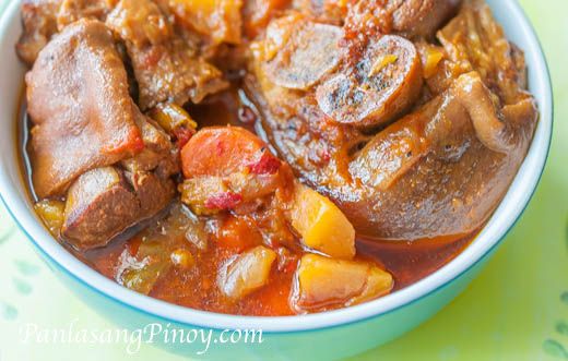 a bowl filled with meat and vegetables on top of a green table cloth next to a spoon