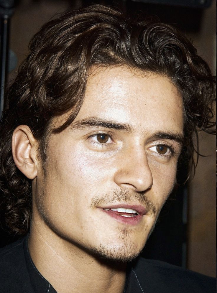 a close up of a person wearing a black shirt and tie with curly hair on his head