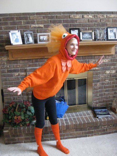 a woman in an orange costume is standing near a fireplace with her arms outstretched and legs spread out