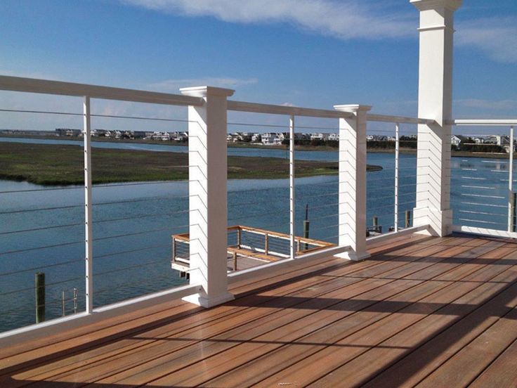 a wooden deck with white railings next to the water