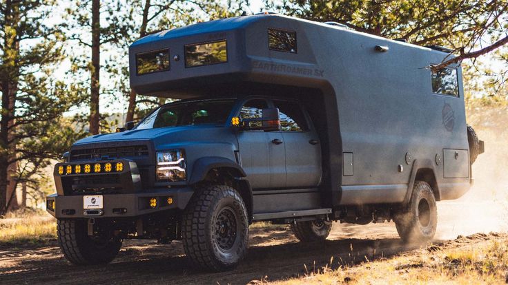 a truck with a tent on the back driving down a dirt road in the woods