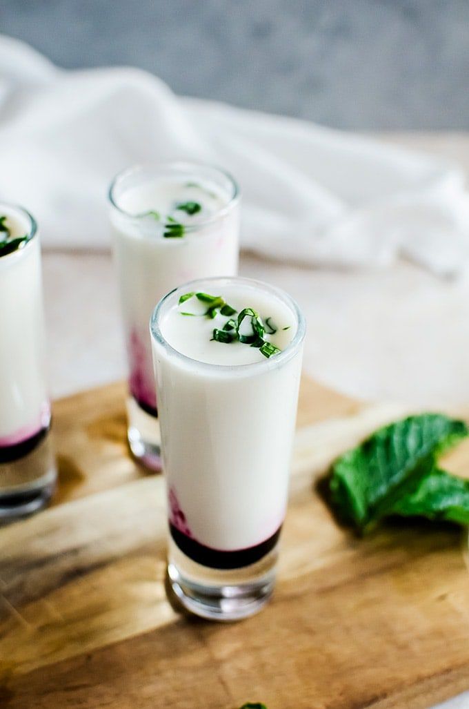 three glasses filled with liquid sitting on top of a wooden cutting board next to green leaves