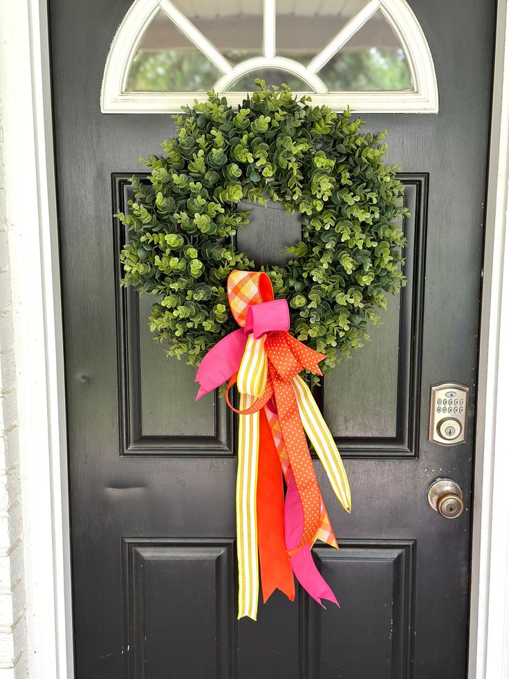 a black door with a green wreath and pink bow on it's front door