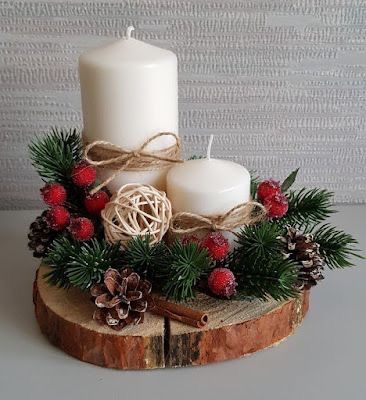 two white candles sitting on top of a piece of wood next to pine cones and berries