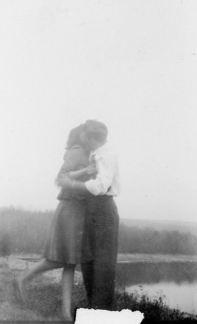 an old black and white photo of two people hugging each other in front of a body of water