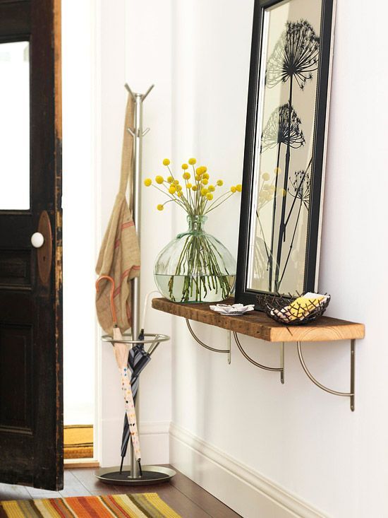 a vase with yellow flowers sitting on a shelf next to a mirror and coat rack