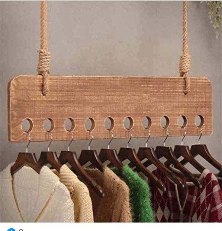 a wooden coat rack with several coats hanging from it's hooks and some sweaters on hangers