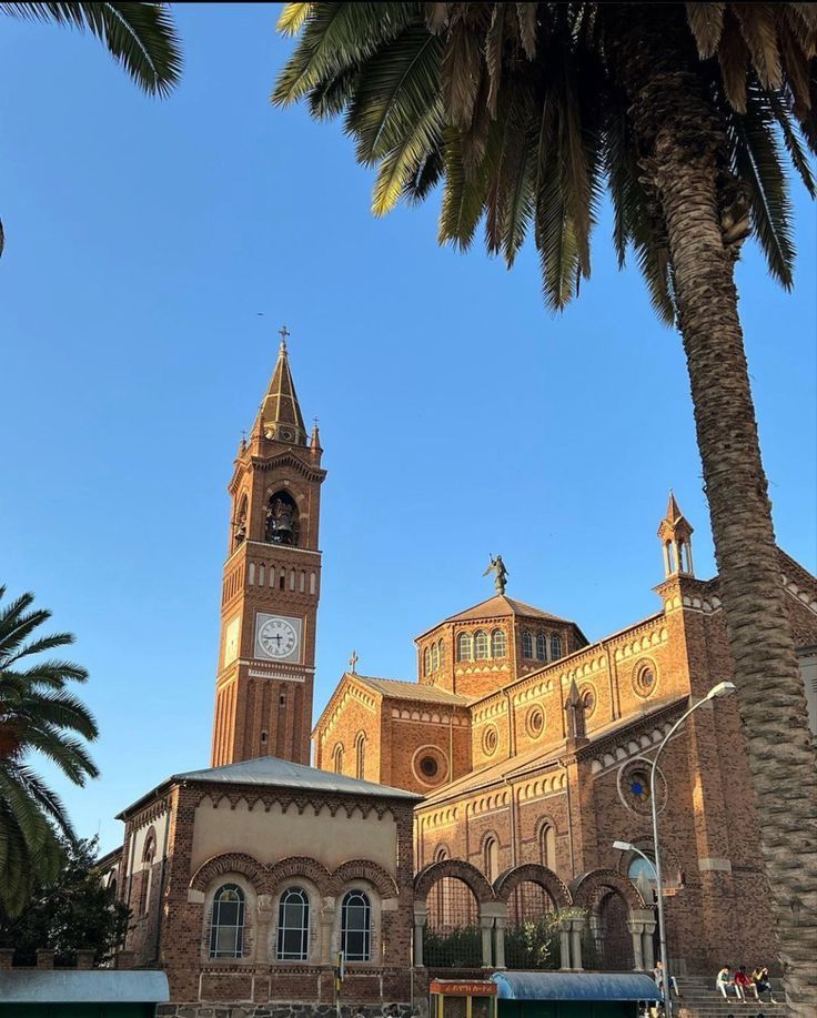 an old building with a clock tower and palm trees in the foreground on a sunny day