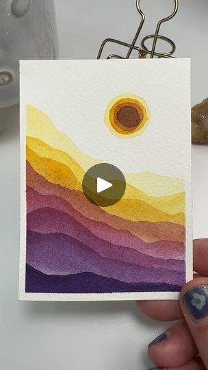 a person holding up a card with an image of the sun on it and mountains in the background