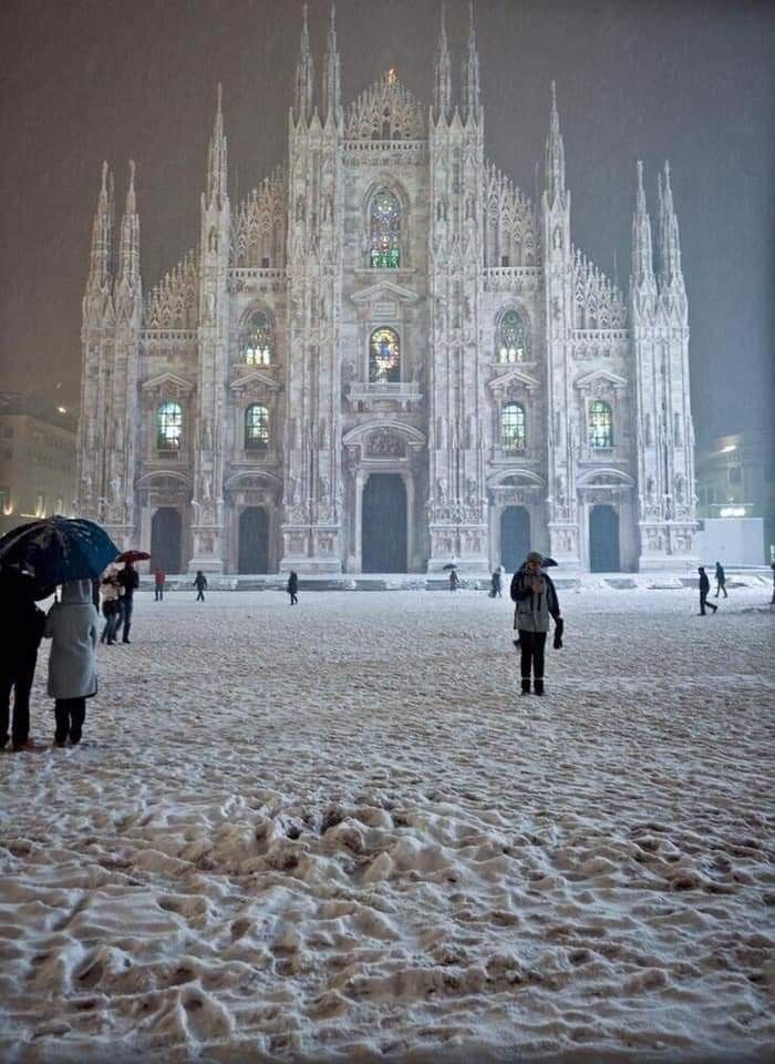 people walking in the snow with umbrellas near a cathedral at night, while it's snowing