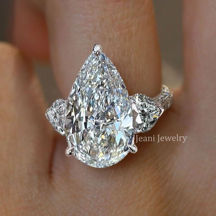 a woman's engagement ring with three pear shaped diamonds on the band and an oval diamond