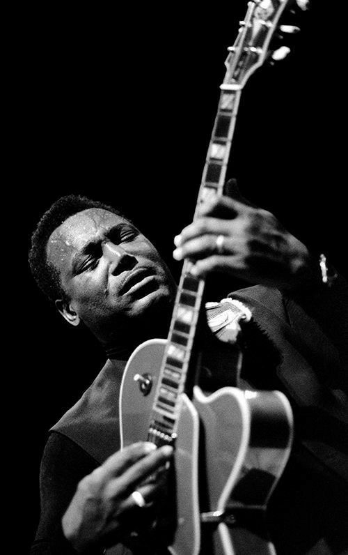 a man holding a guitar in his right hand and looking up at the sky with one eye open