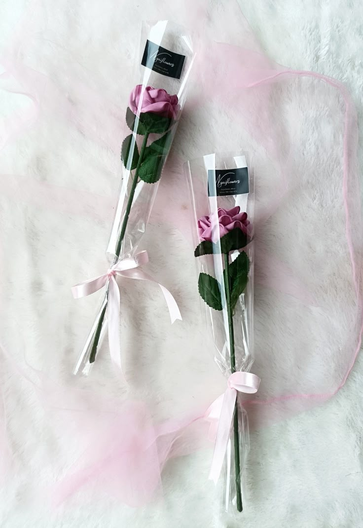 two pink roses wrapped in clear cellophane and tied with ribbon on white furnishing