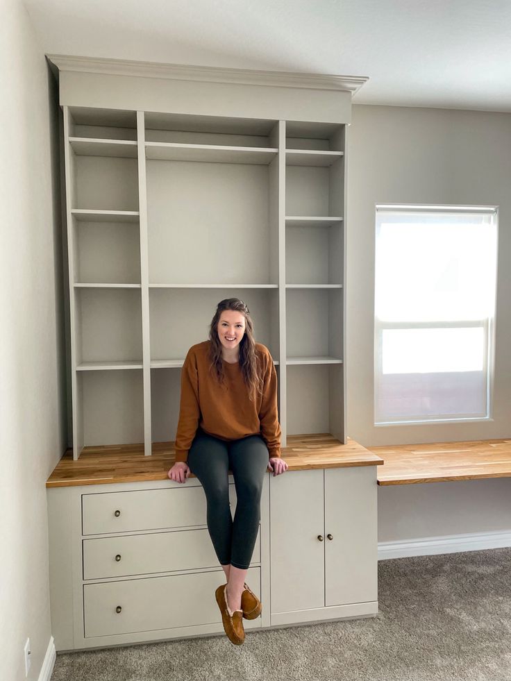 a woman sitting on top of a bookcase in a room with carpeted floors