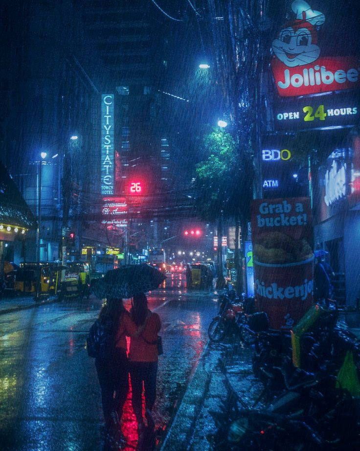 two people walking down the street in the rain at night with an umbrella over their head