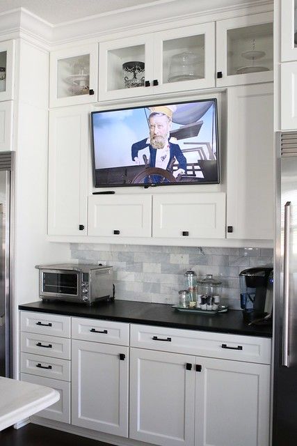 a kitchen with white cabinets and black counter tops has a large television on the wall