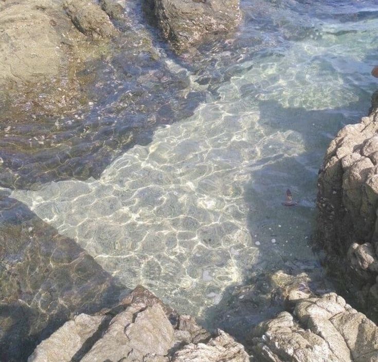 a man standing on top of a rocky cliff next to the ocean with his feet in the water