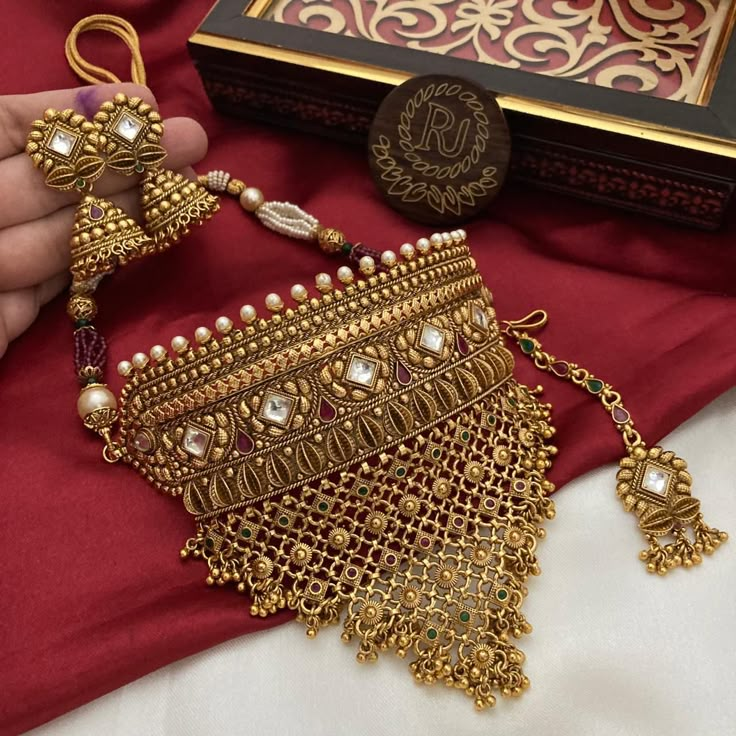 a person is holding a gold necklace with pearls on it and an ornate box in the background