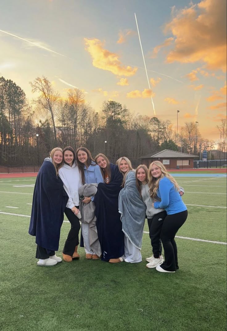 a group of women standing next to each other on top of a grass covered field