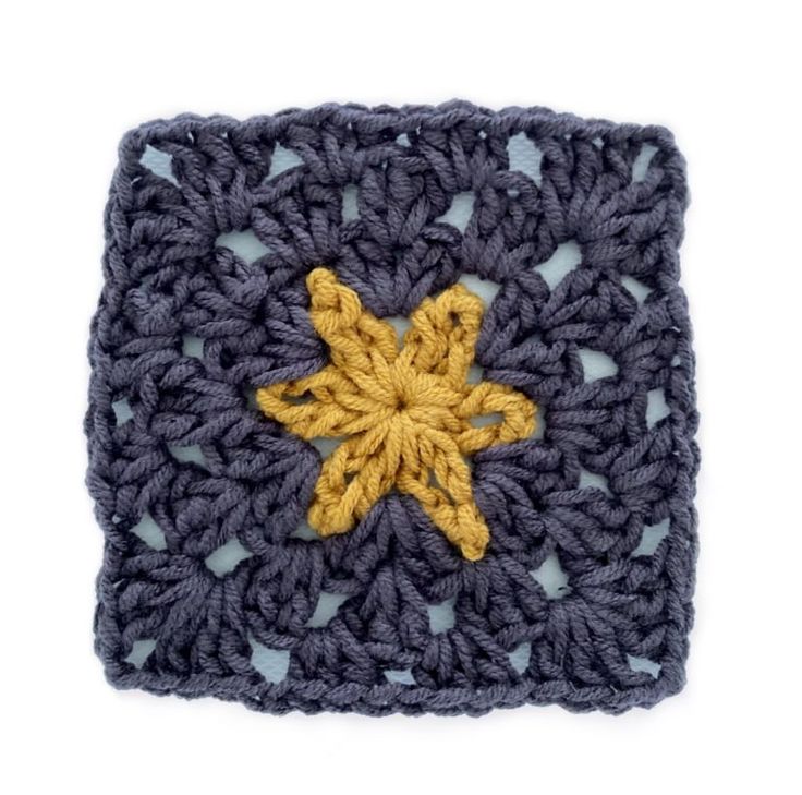 a crocheted square with a yellow star on it's center and blue yarn