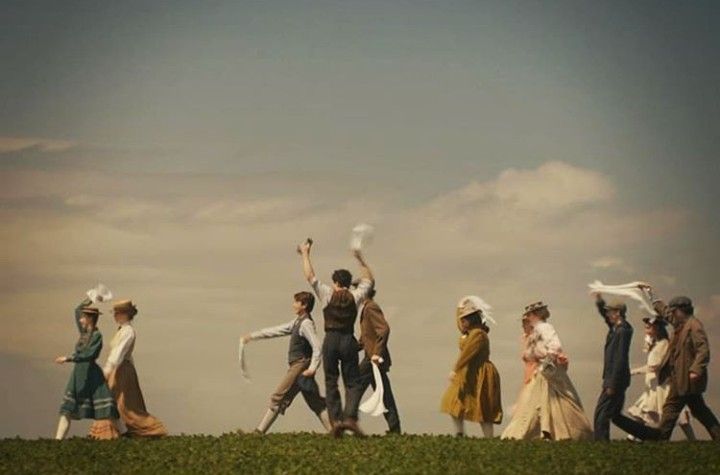 a group of people walking across a grass covered field next to each other on a cloudy day