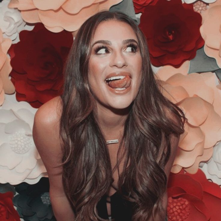 a woman with long brown hair is posing in front of red and white paper flowers