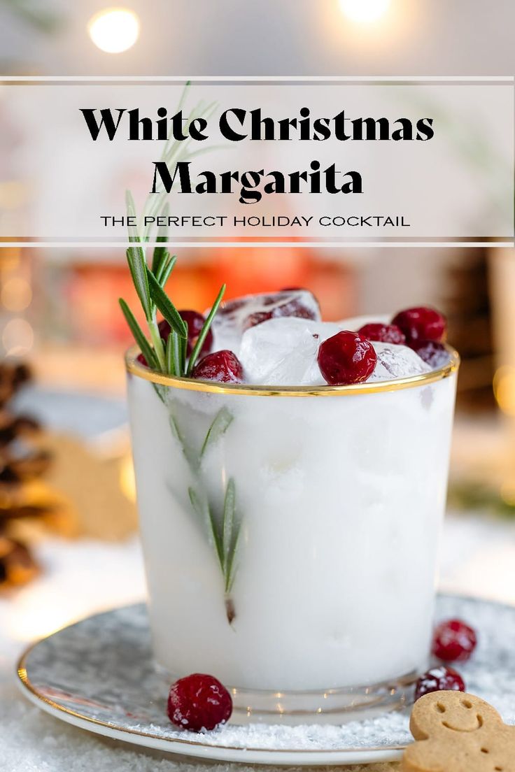 white christmas margarita in a glass with ice and cranberries on the rim next to a cookie