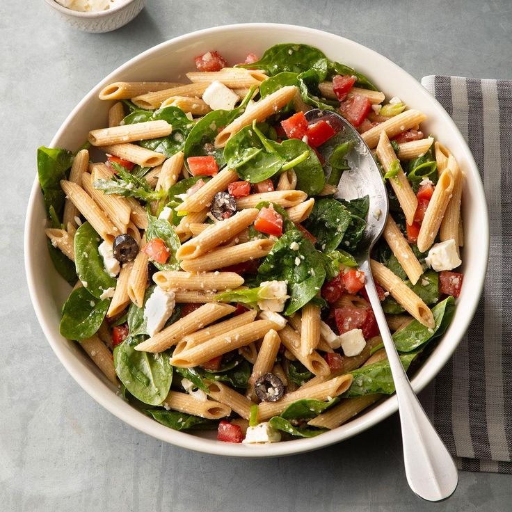 a white bowl filled with pasta salad next to a cup of sauce and a spoon